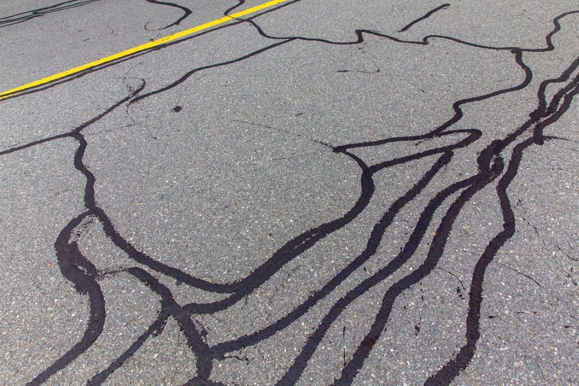 Asphalt pavement with dark, tar-filled cracks. A yellow line is visible in the upper left.