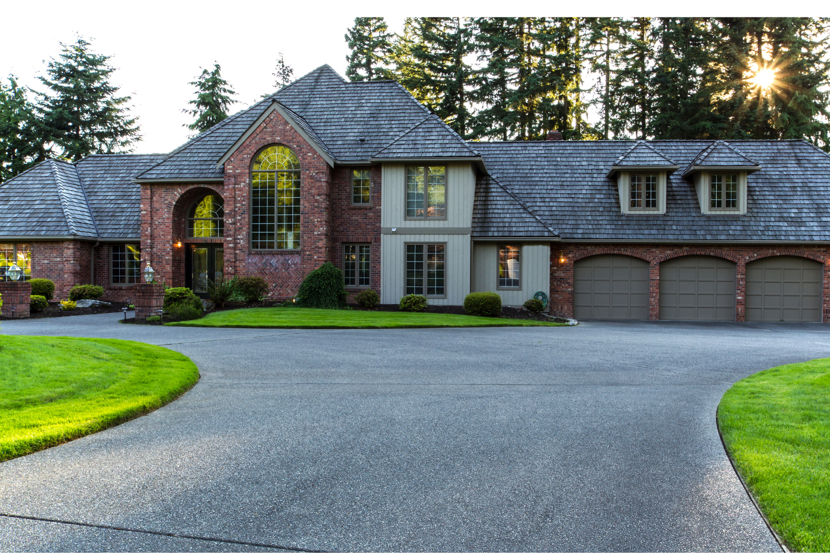 A large brick house with a three-car garage and red front door, set on a concrete driveway under a blue sky.