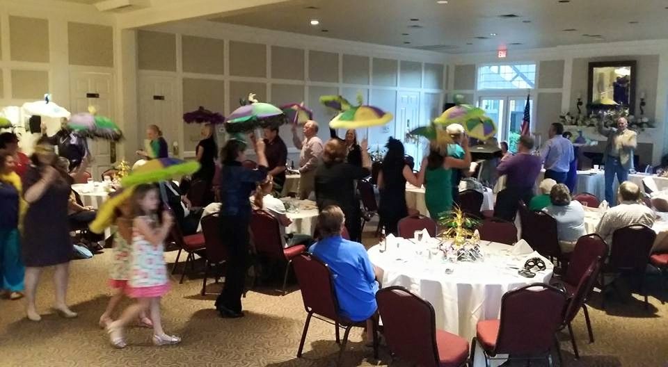 A group of people are dancing in a room with tables and chairs.