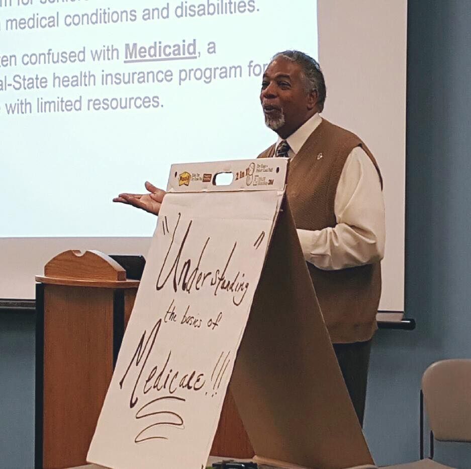 A man stands at a podium giving a presentation on medicaid