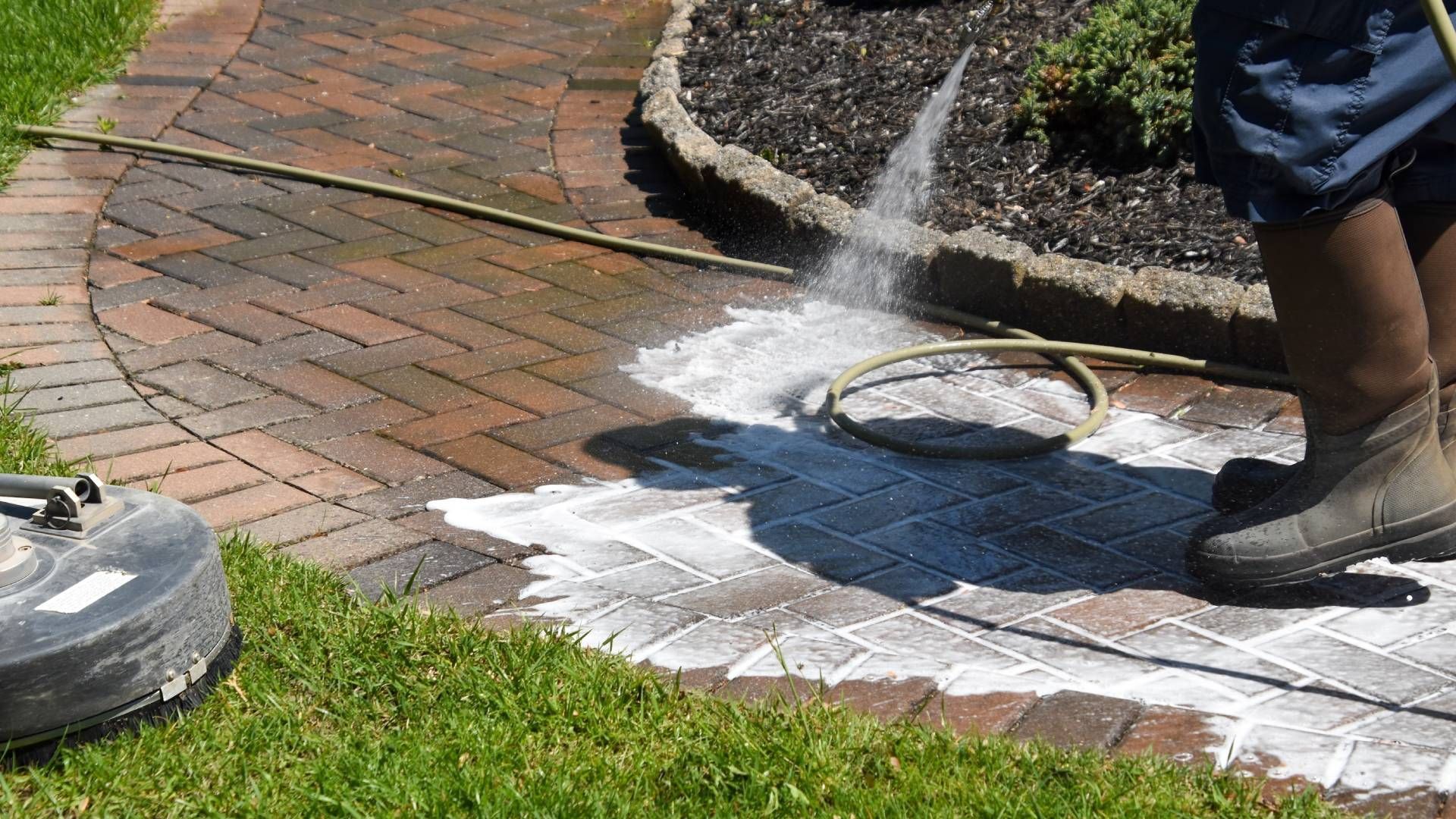 A person is cleaning a brick walkway with a pressure washer.