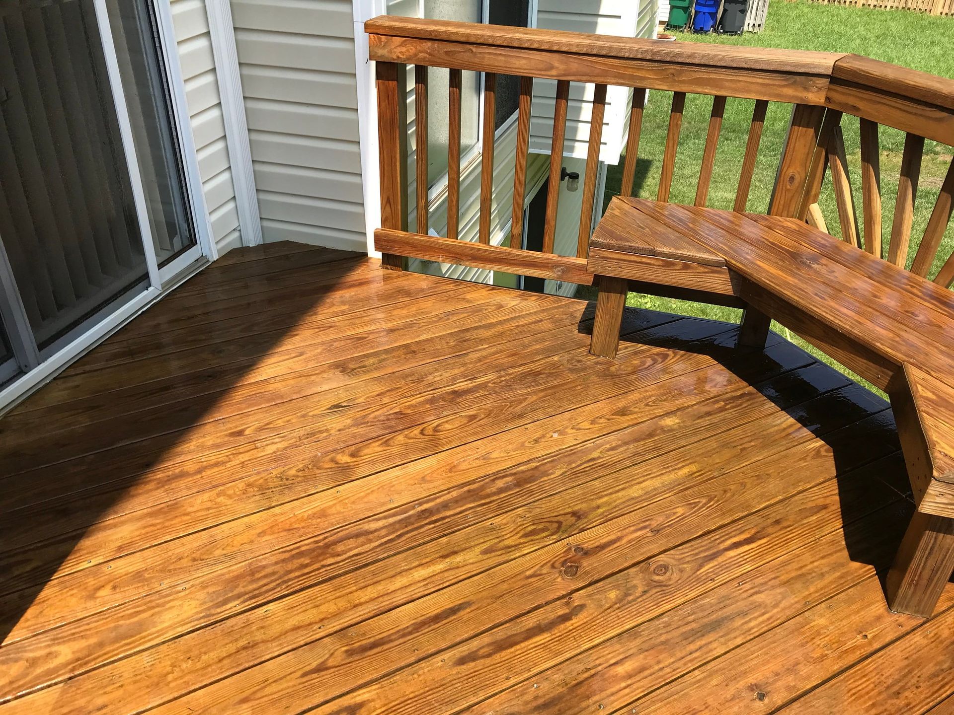 A wooden deck with a bench and railing in front of a house.