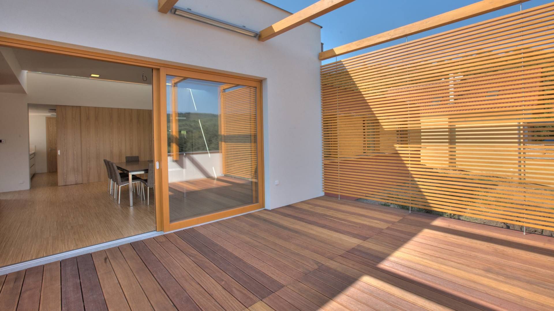 A wooden deck with a sliding glass door leading to a dining room.