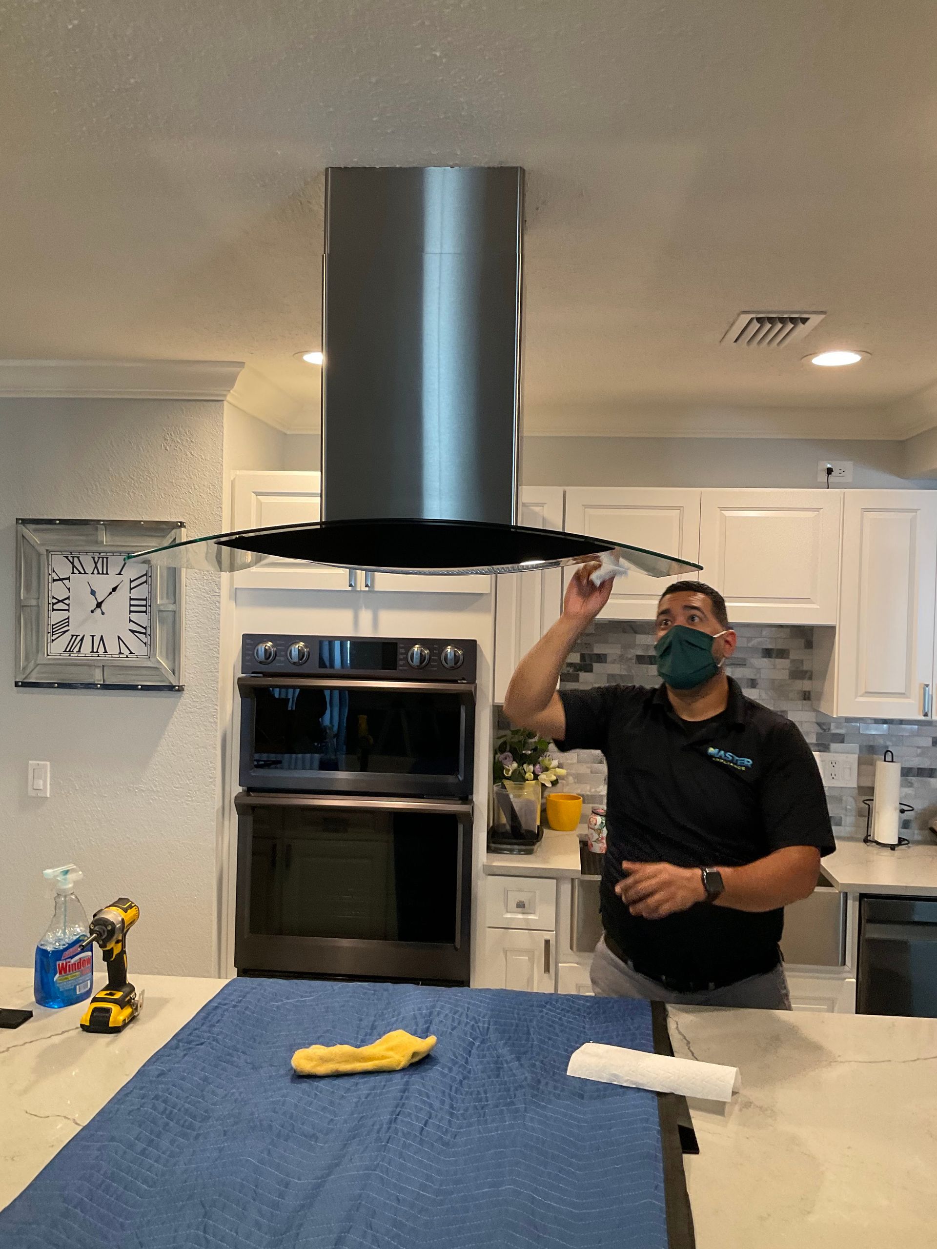 A man wearing a mask is standing in a kitchen looking at a stove hood.
