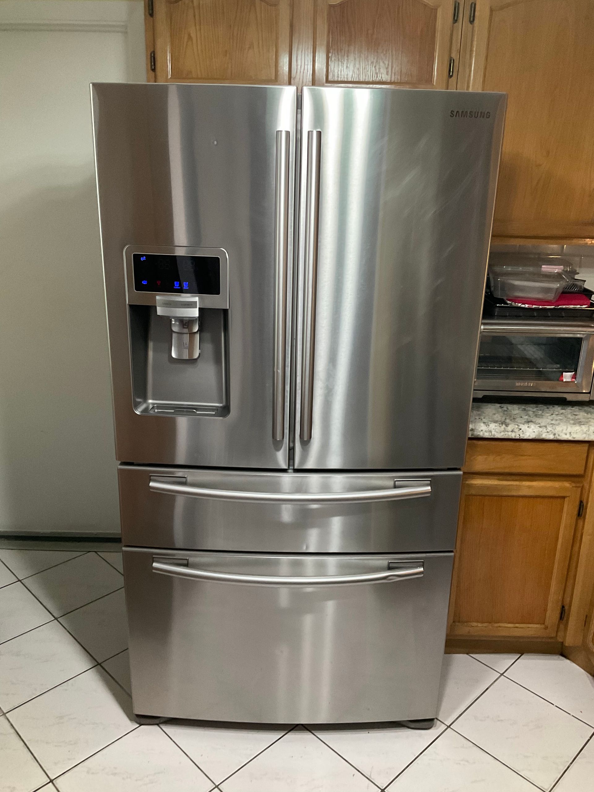A stainless steel refrigerator is sitting on a tiled floor in a kitchen.