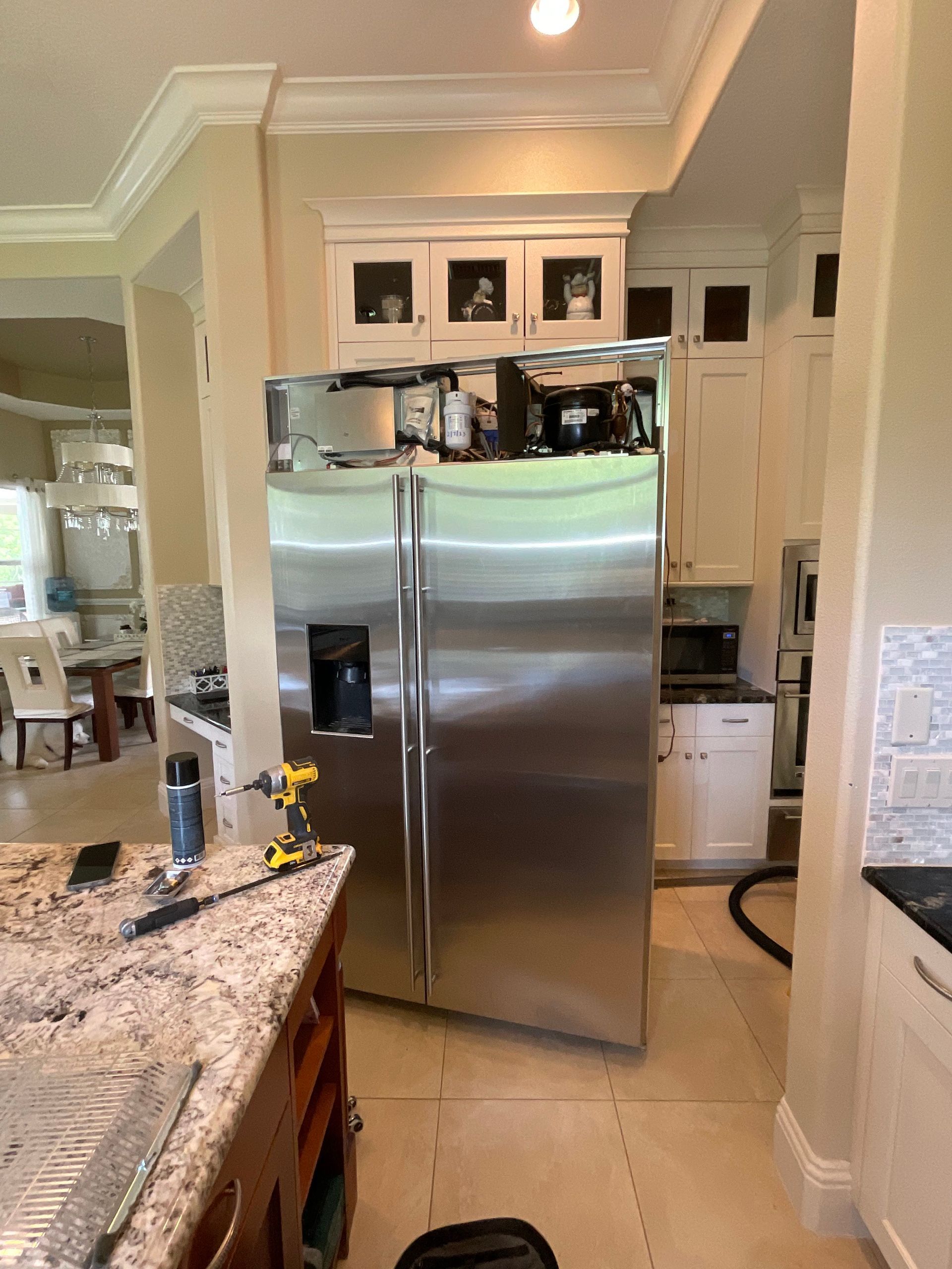 A stainless steel refrigerator is being repaired in a kitchen