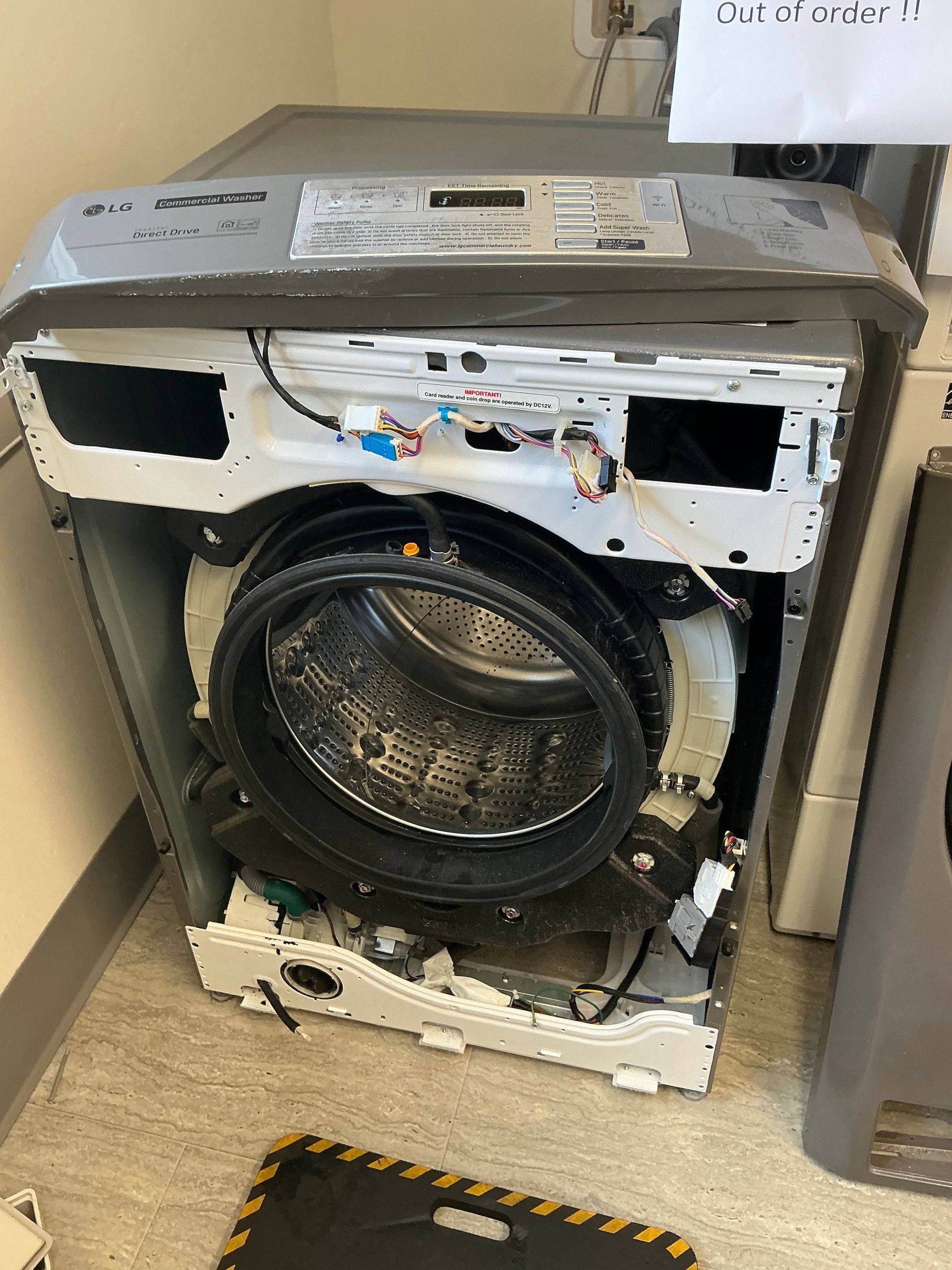 A broken washing machine is sitting on the floor in a laundry room.