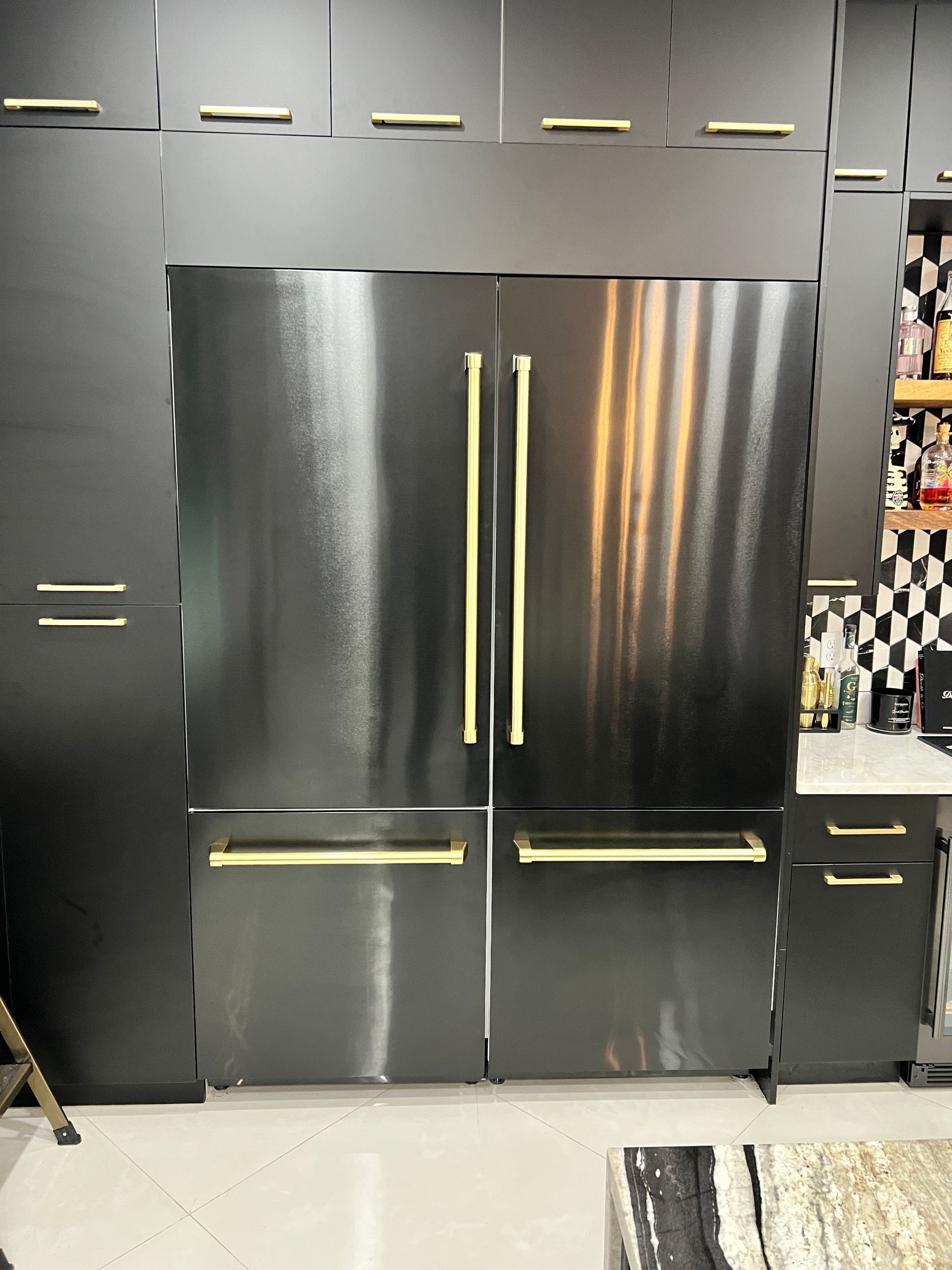 A kitchen with black cabinets and a stainless steel refrigerator