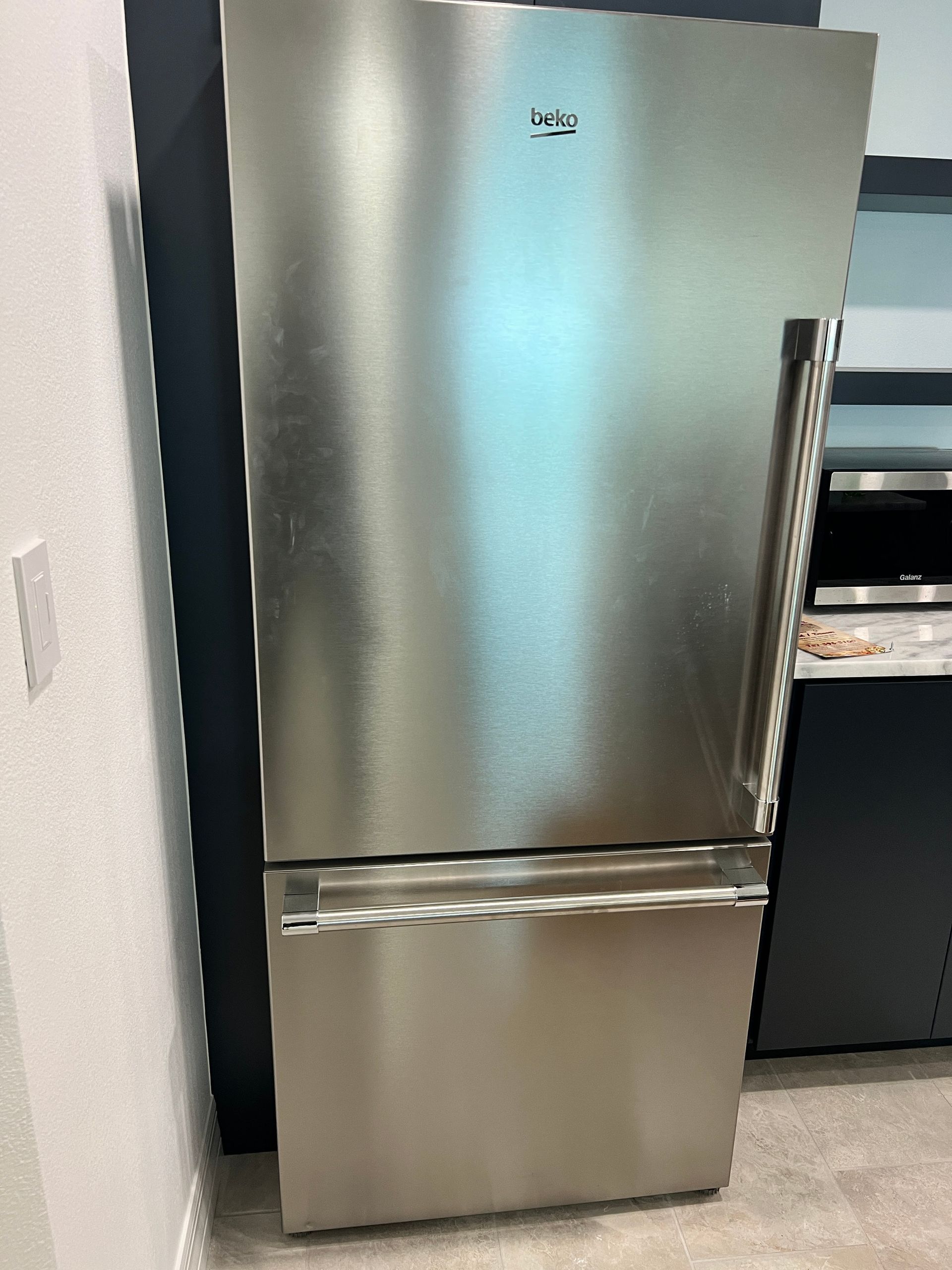 A stainless steel refrigerator is sitting on the floor in a kitchen.