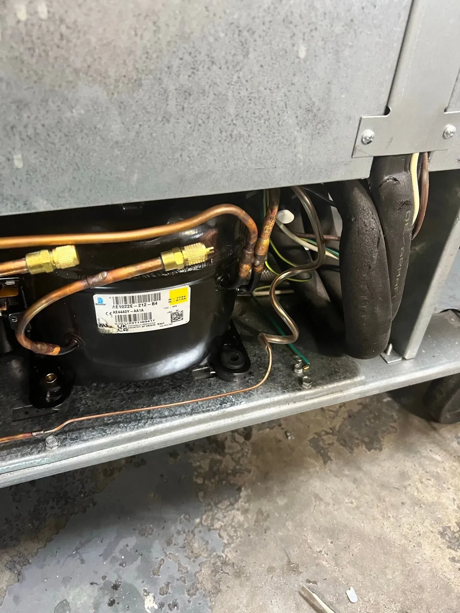 The inside of a refrigerator with a compressor and hose attached to it.