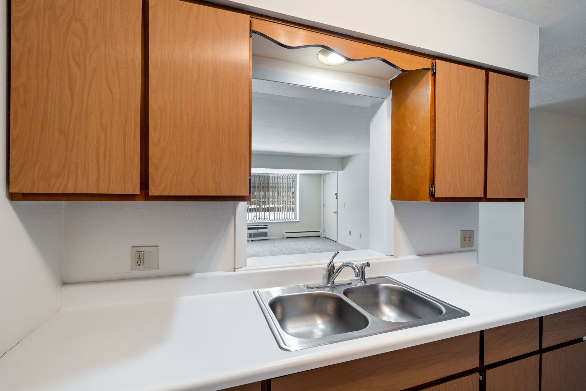 Photo of a kitchen sink at a counter with a small opening that looks out to the living room