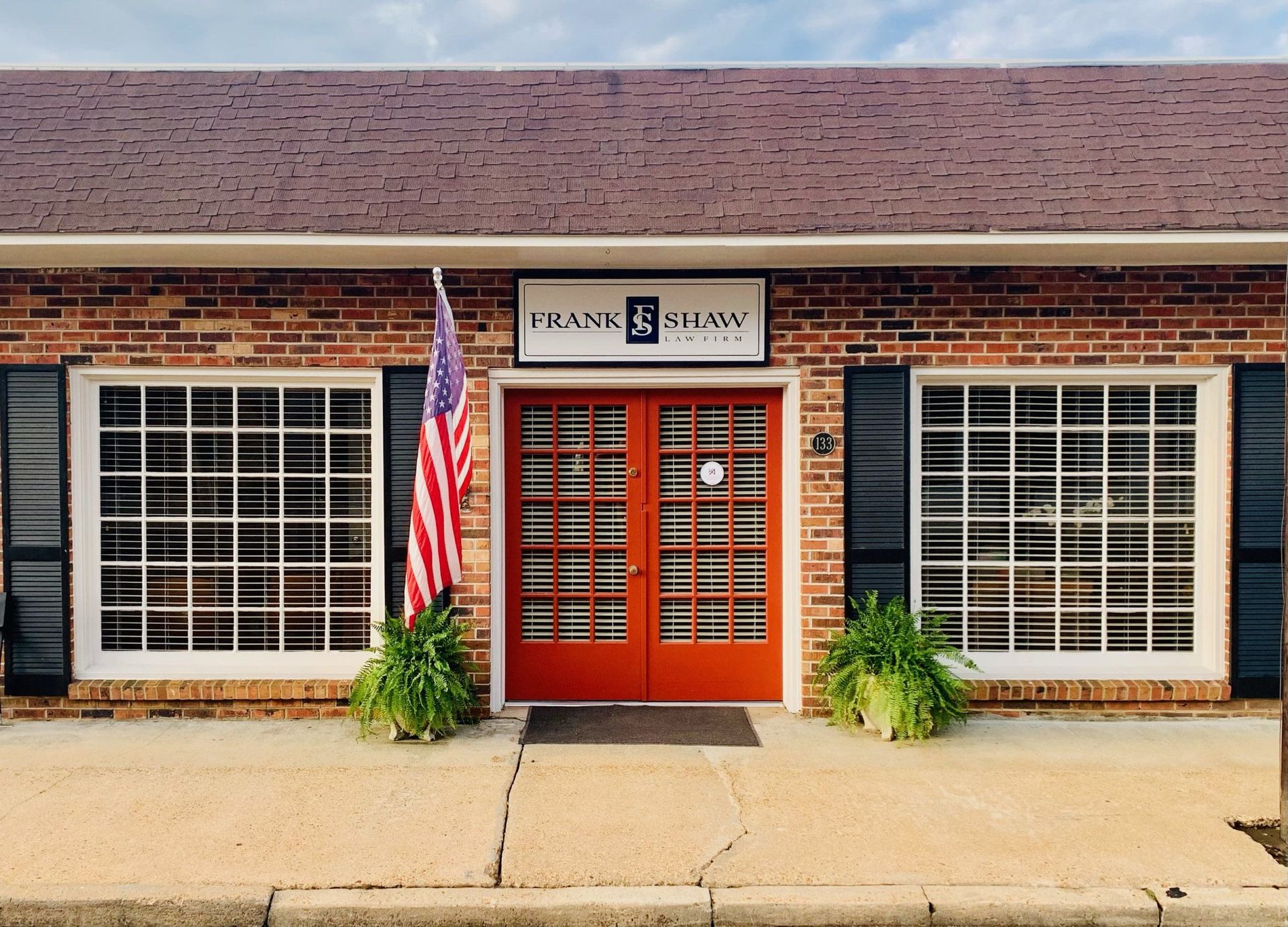 Brick building with red double doors, windows with black shutters, and an American flag.
