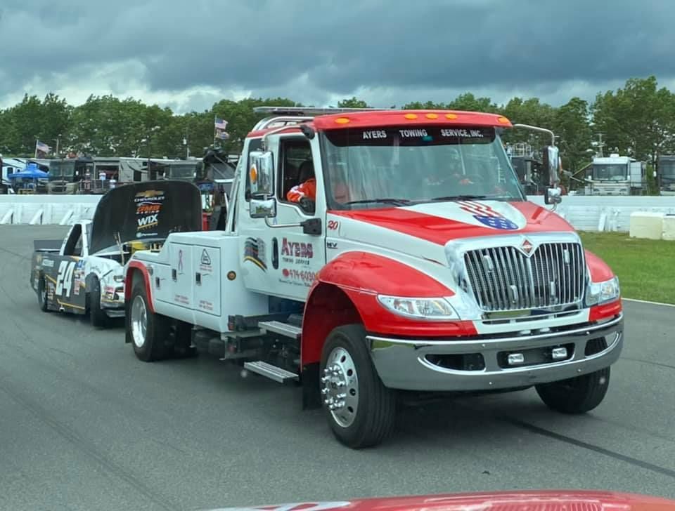 A red and white tow truck is towing a race car on a track.