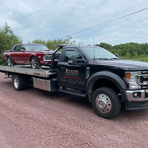 A tow truck is towing a red car on a gravel road.