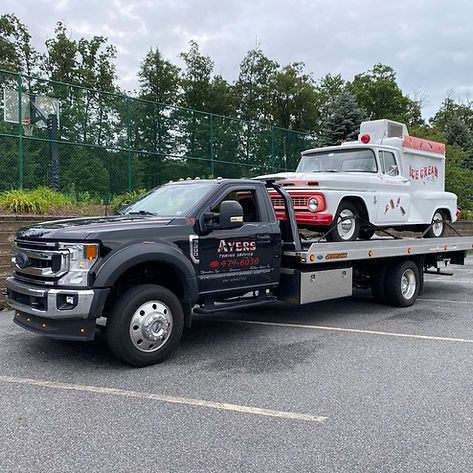 A tow truck is carrying a white truck and a red truck.
