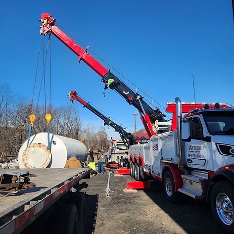 A tow truck is carrying a large tank on a flatbed trailer.