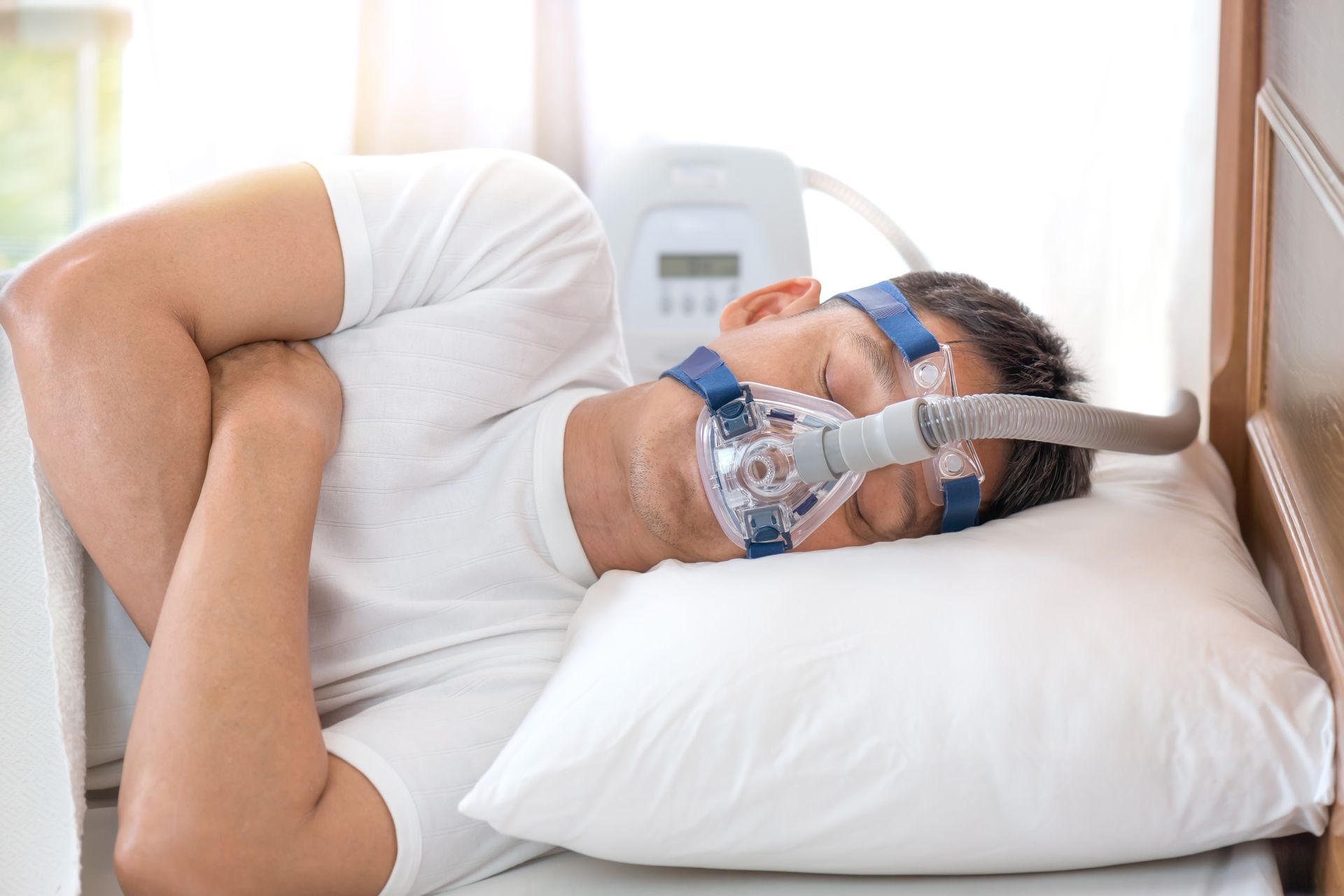 A person sleeping on their side in a white bed while wearing a CPAP mask connected to a machine.