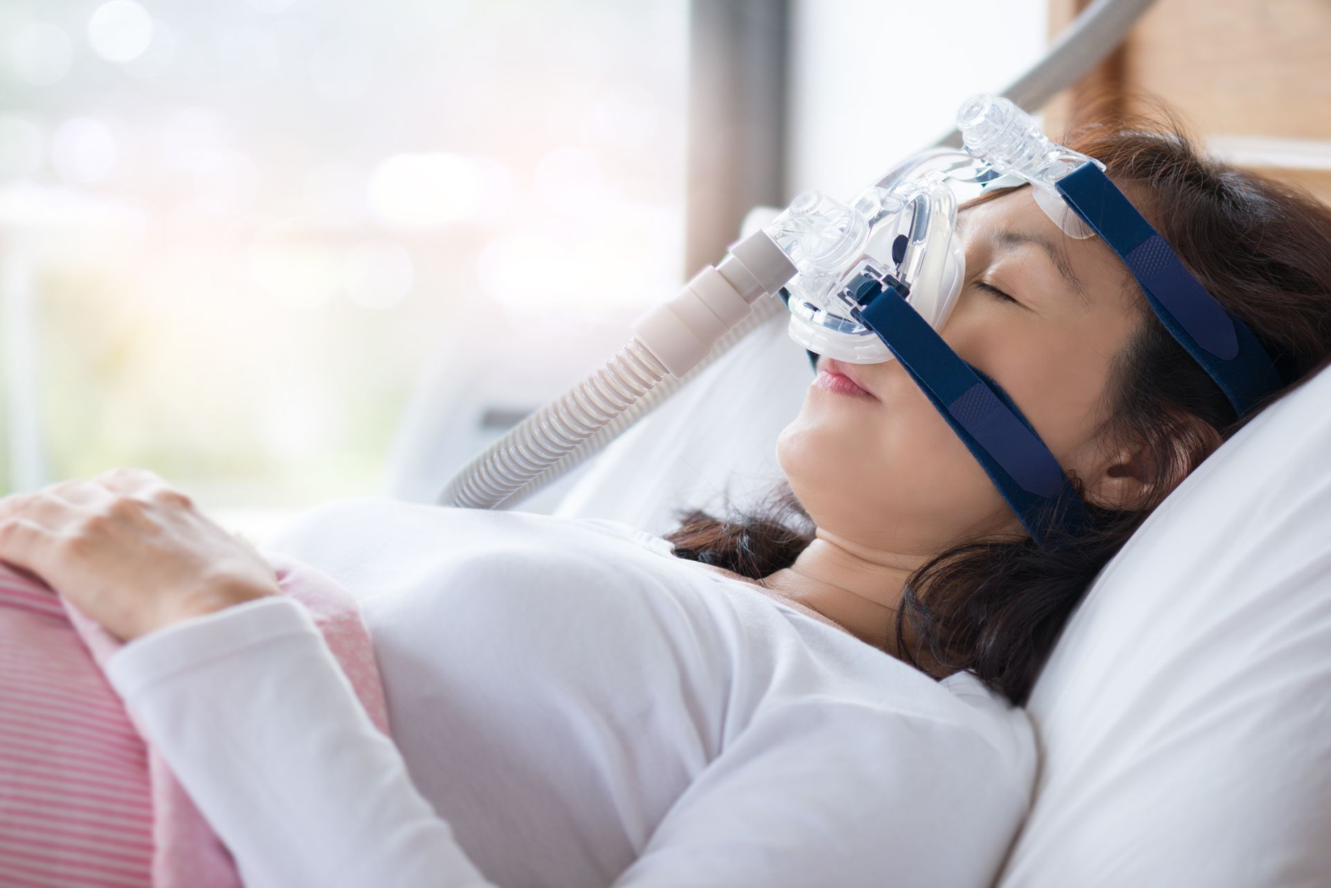 A person sleeping in a bed while wearing a CPAP mask connected to a breathing machine.