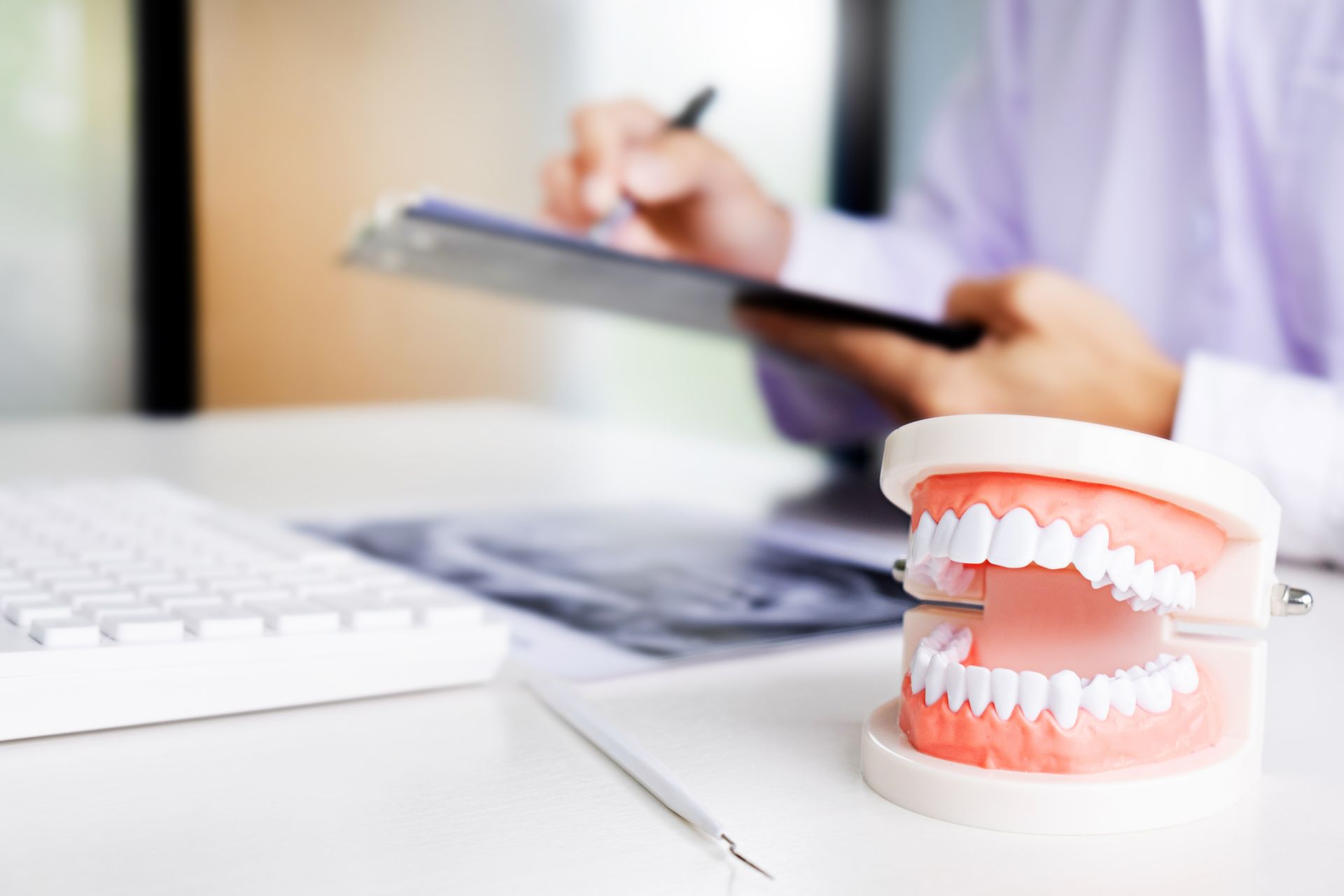 A dental model of human teeth sits on a desk in front of a professional writing on a clipboard.