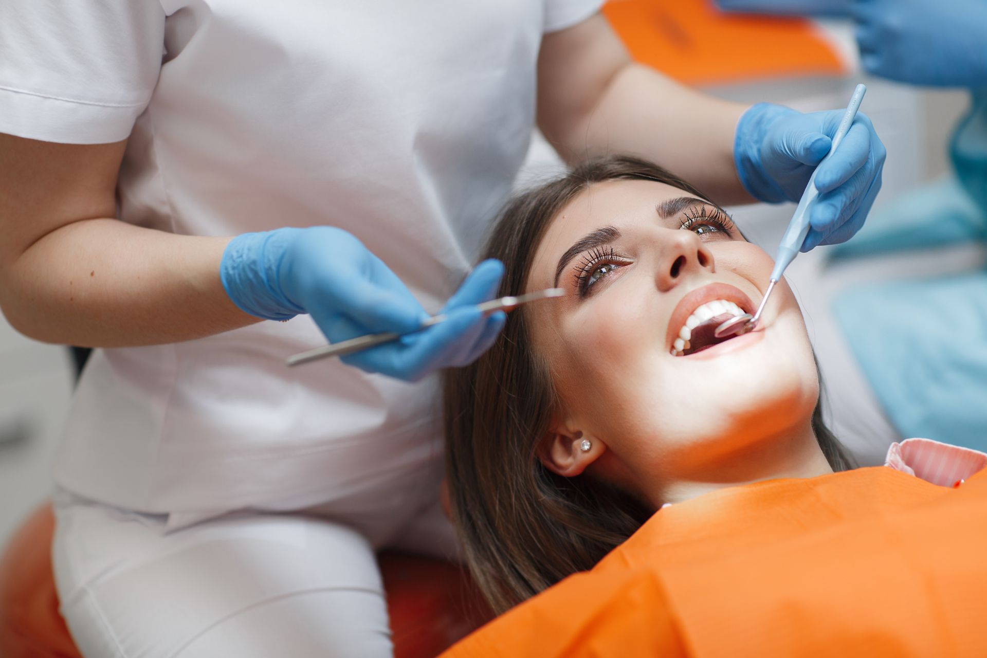 A dentist performing an oral exam on a patient wearing an orange bib in a clinical setting.