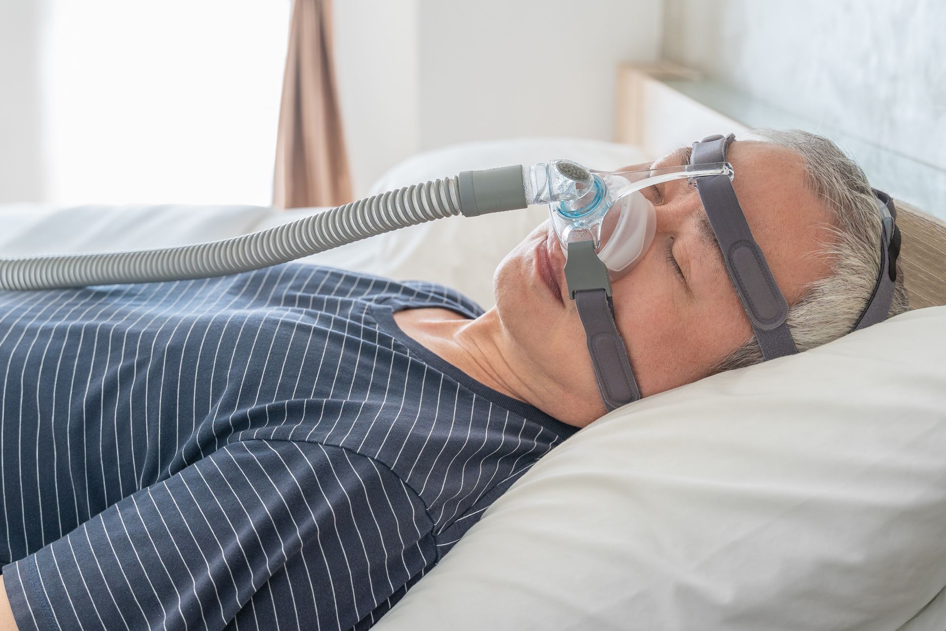 A person sleeping in bed wearing a CPAP nasal mask and headgear connected to an air tube.
