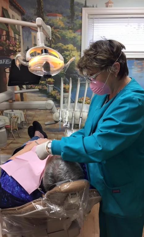 A dental professional wearing blue gloves uses a dental handpiece to polish a patient's teeth.