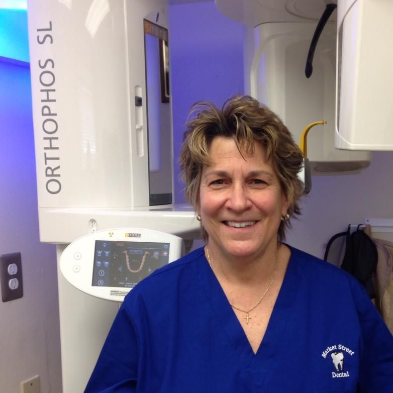 A dentist wearing a mask and blue gloves consults with a patient sitting in a dental chair in a bright, modern office.