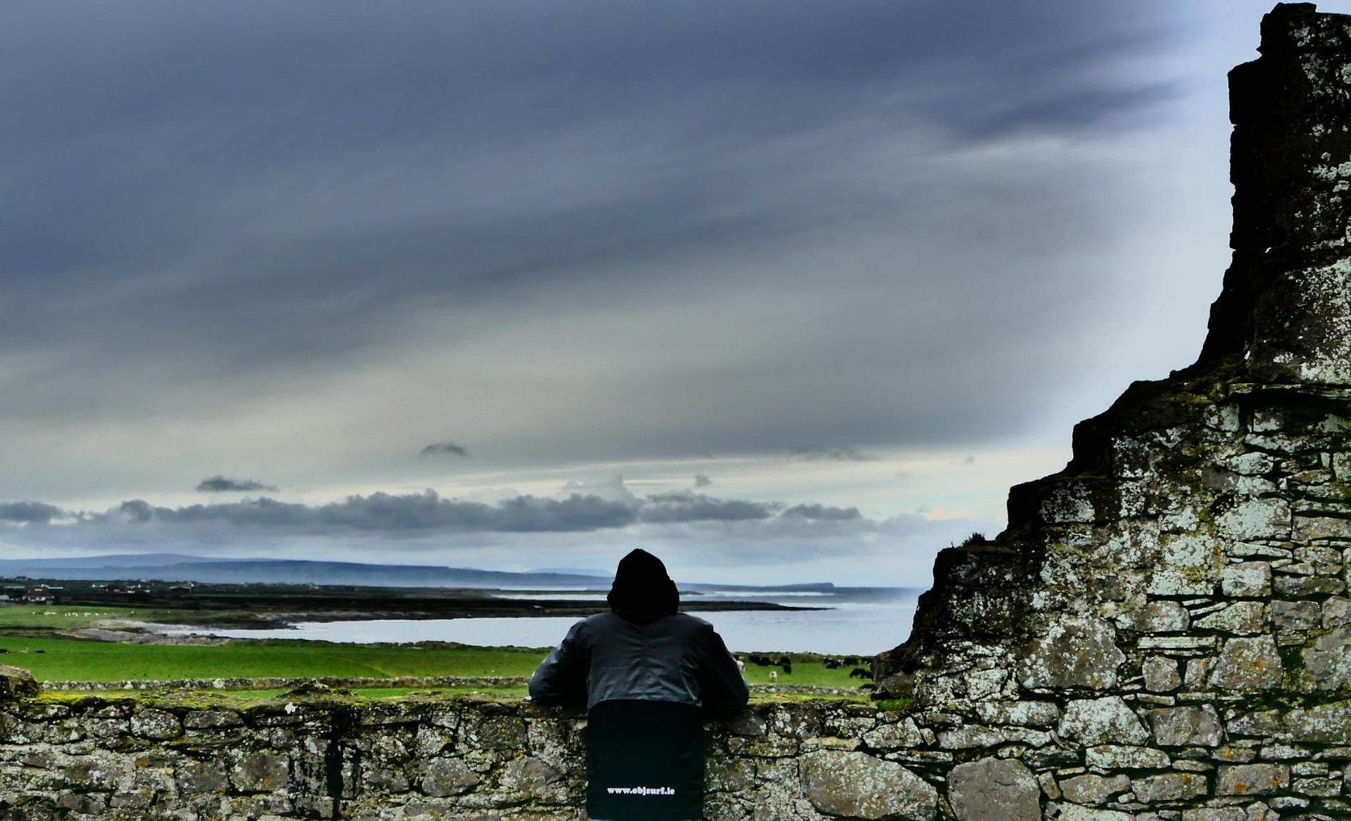 A person standing on a stone wall overlooking a body of water