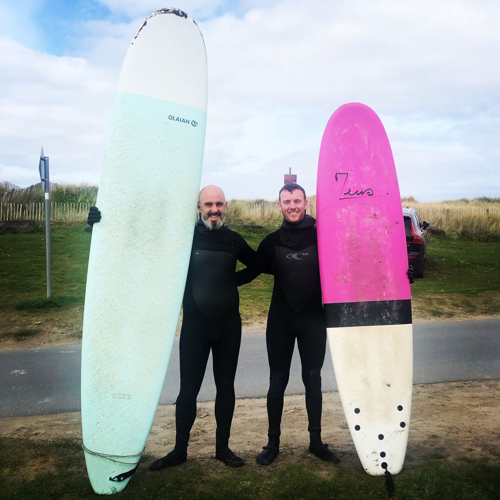 Two men standing next to each other holding surfboards