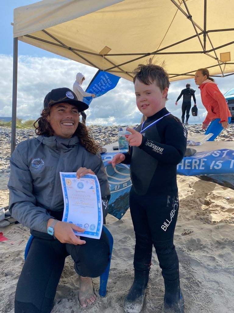 A man is giving a certificate to a young boy on the beach.
