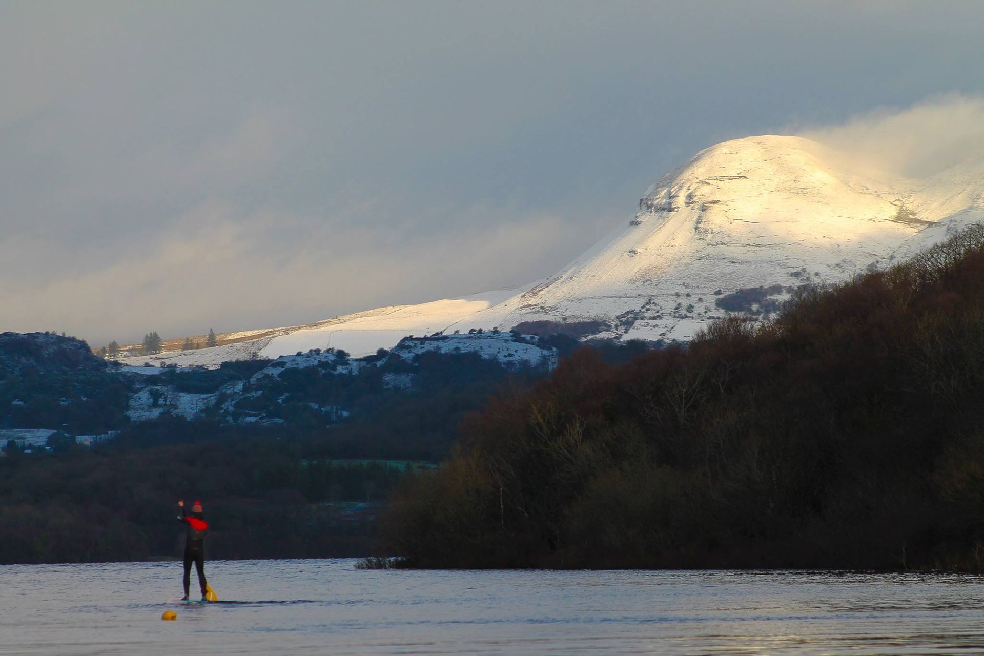 A person is standing on a paddle board in front of a snowy mountain.
