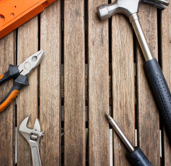 Assorted hand tools on weathered wooden boards, including pliers, wrenches, and a hammer