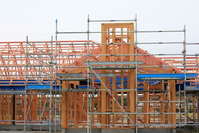 Partially built house with wooden framing and scaffolding under a red roof in an active construction site