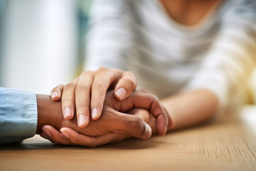 Hands gently clasped together on a wooden table in a soft, supportive setting