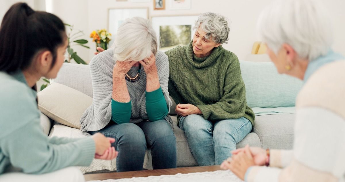 Counselor speaking with a distressed woman and supportive companion in a bright living room counseling session