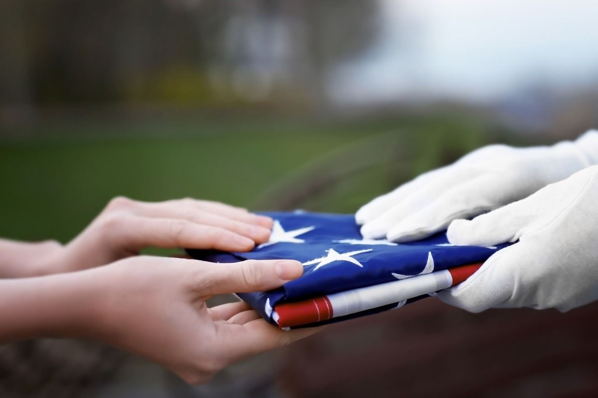 Hands exchanging a folded American flag outdoors