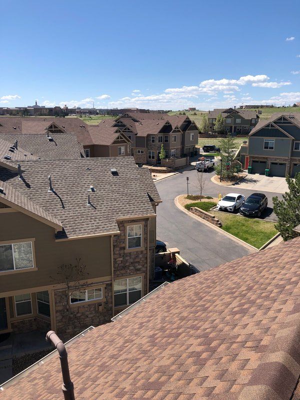 View of residential neighborhood, brown roofs, street, cars, and green space under blue sky.