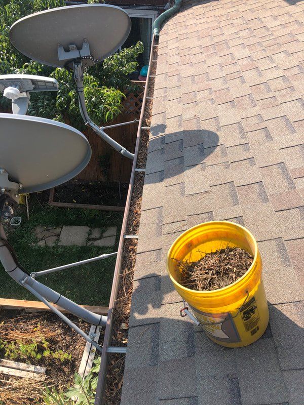 A yellow bucket of debris next to a gutter on a rooftop with satellite dishes.