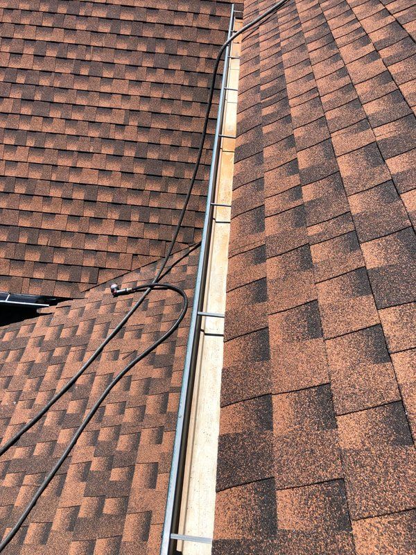 Close-up of a brown shingled roof with a metal gutter and attached cable running down the center.