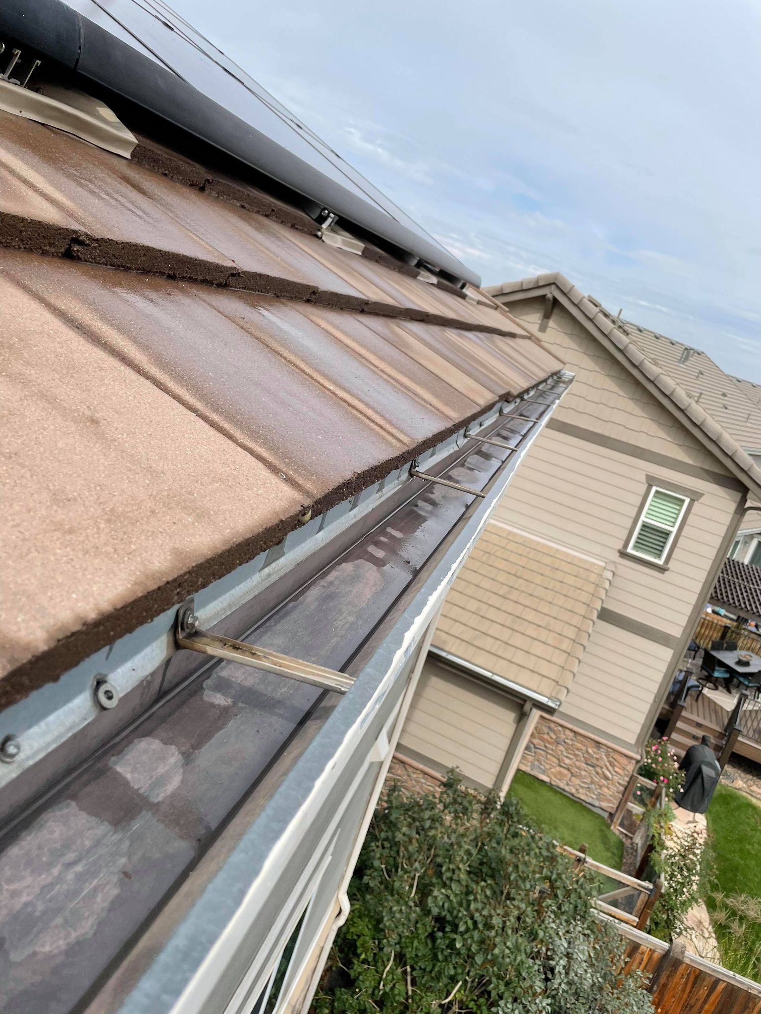 View of a house roof with a gutter, solar panels, and a glimpse of the yard.