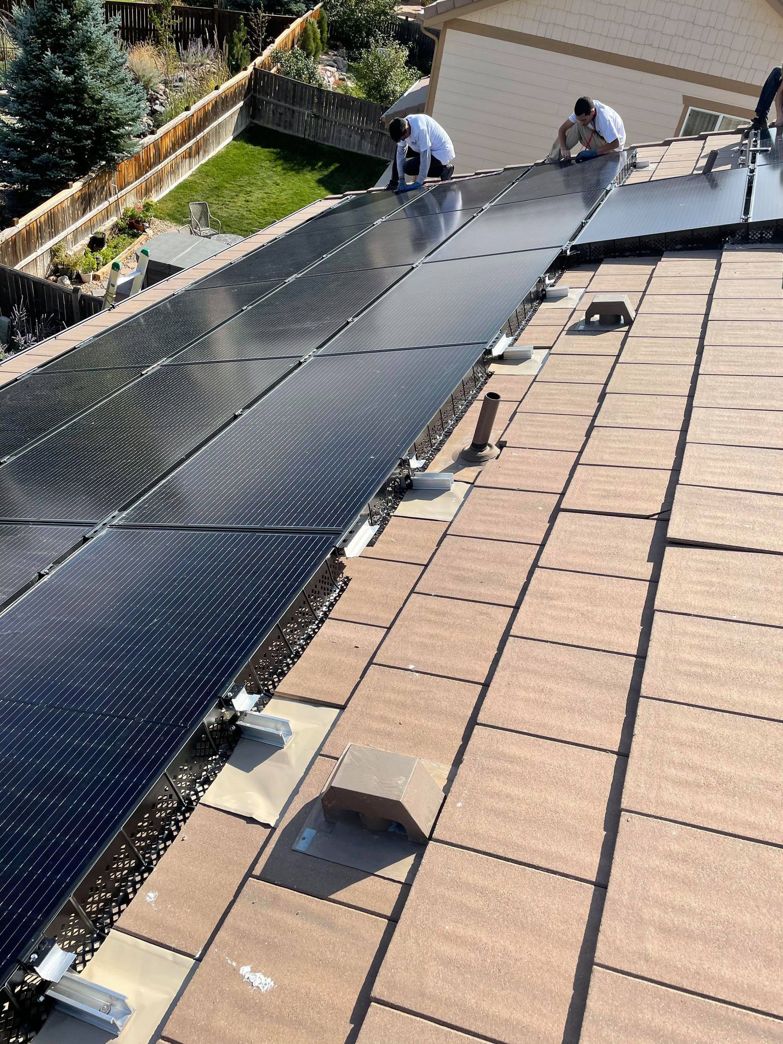 Workers installing solar panels on a brown shingle roof; sunny day.