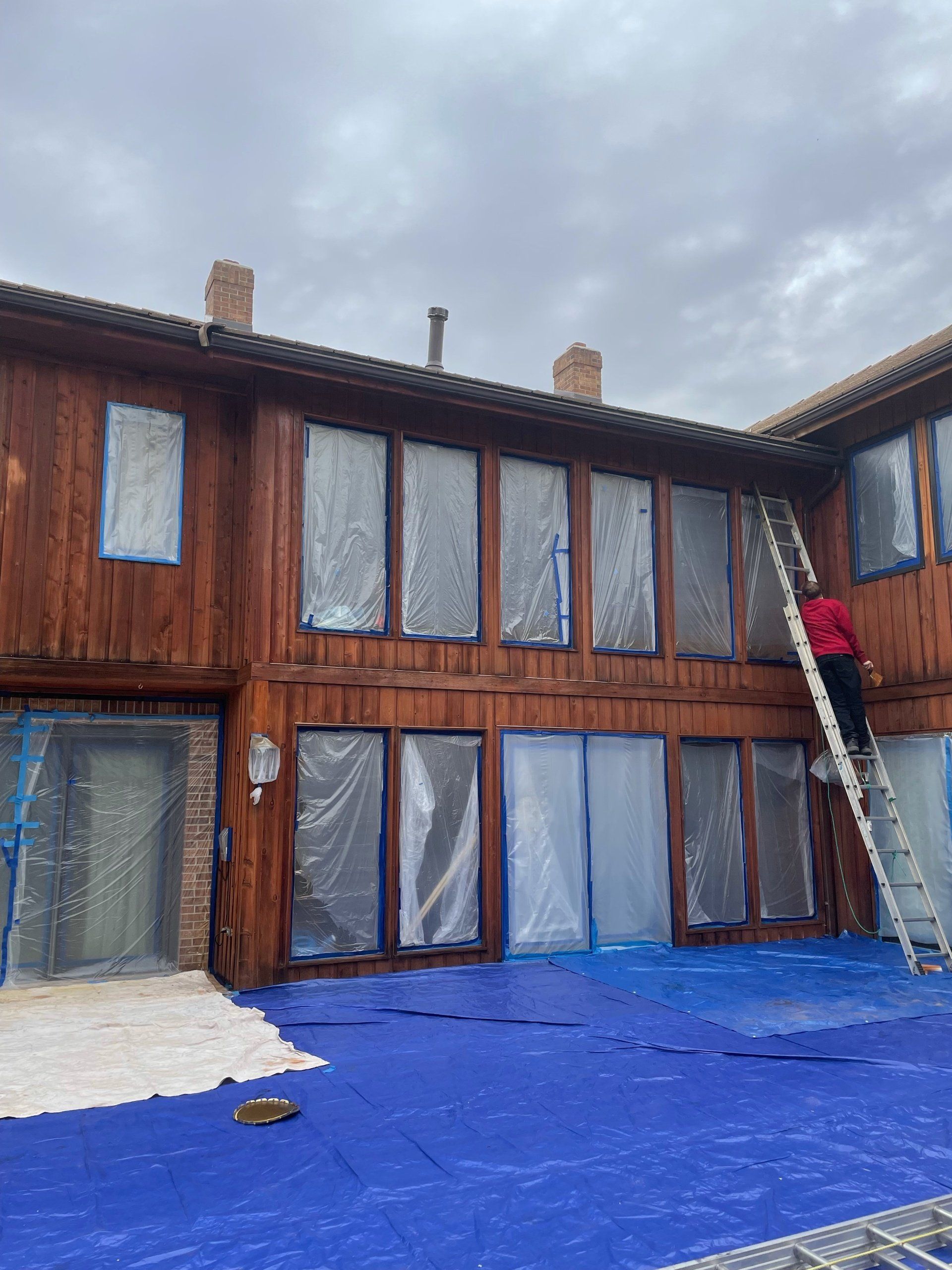 A man is standing on a ladder in front of a wooden house.