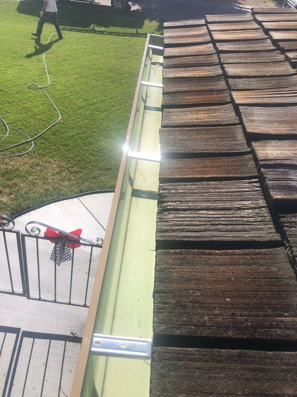 Gutter on a roof with a person walking in the background on the grass.