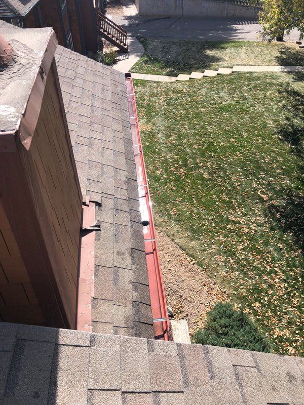 A rooftop with shingles and a gutter, overlooking a grassy yard with a sidewalk.