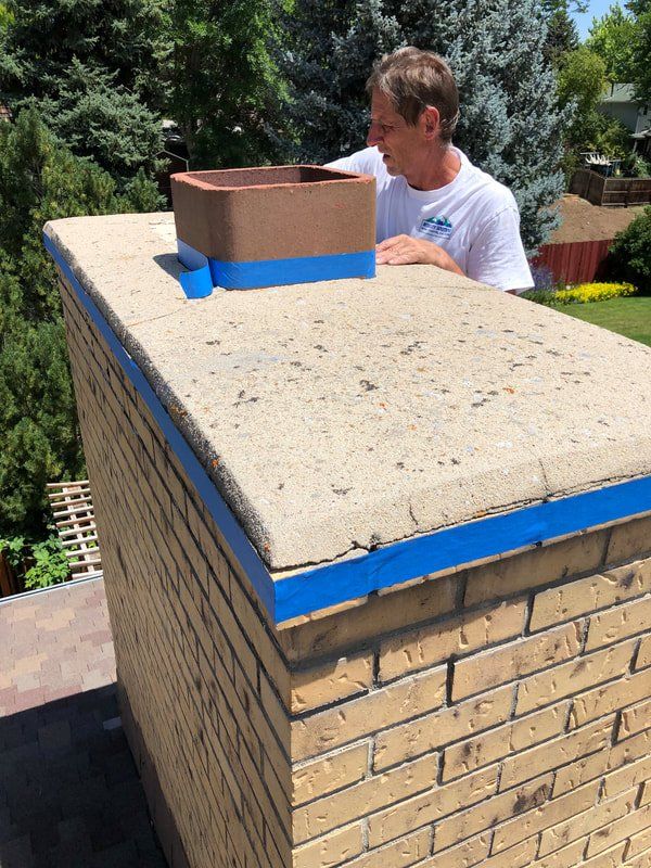 Man working on a chimney, taping the cap. Blue tape outlines the chimney top.
