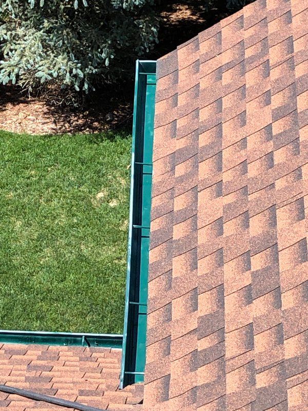Brown shingled roof with a green metal flashing against a green lawn and trees.