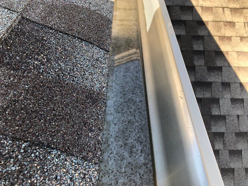 Close-up of a roof's shingles, a gutter, and a flashing, with slight sunlight.