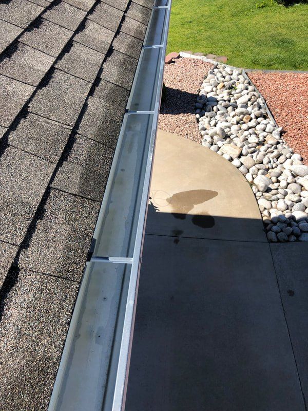 View of roof gutter with shingles, concrete, and landscaping.