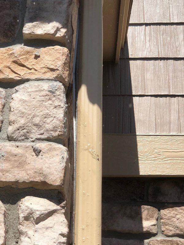 Beige downspout next to a stone wall and cedar shake siding.