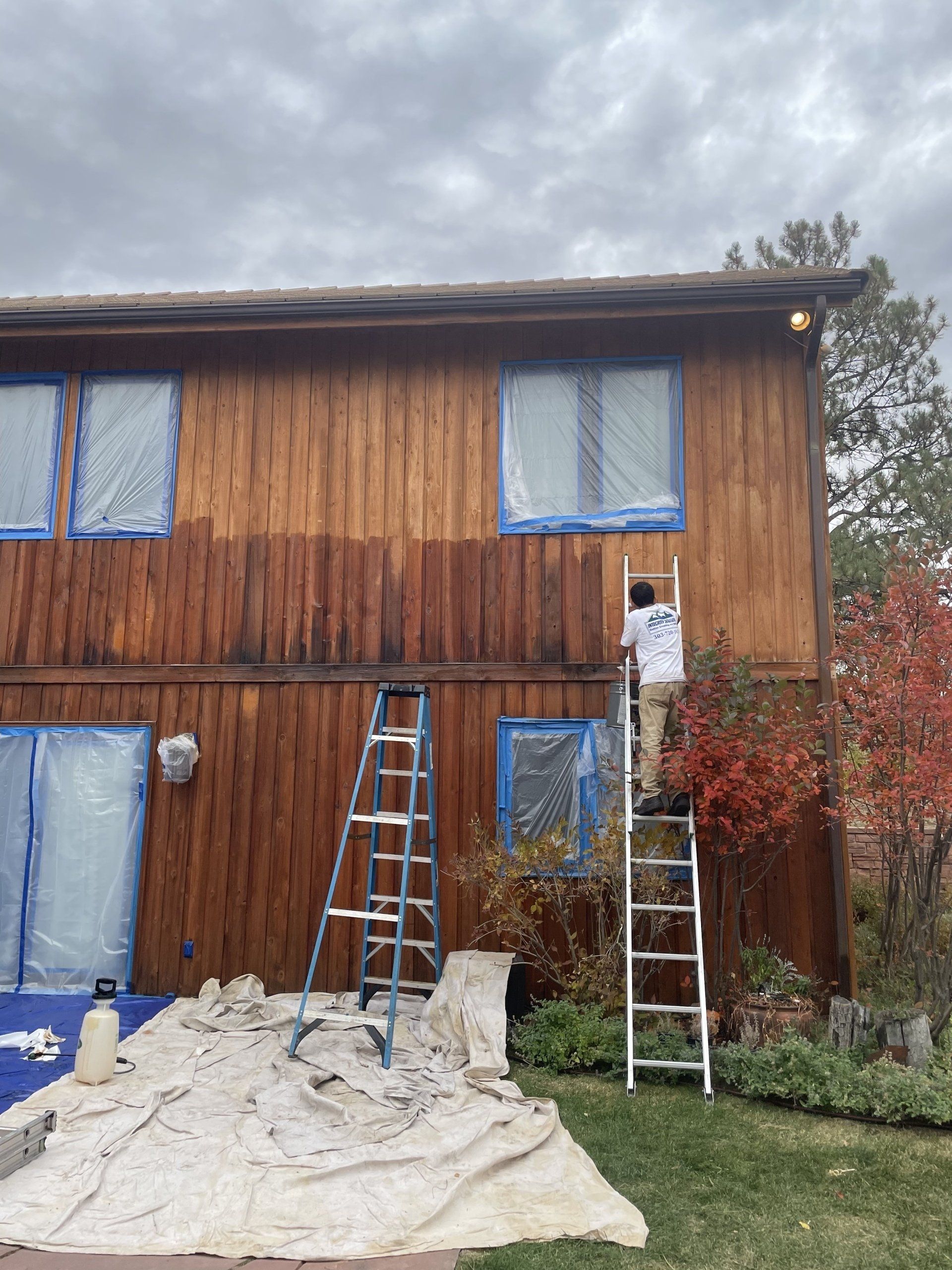 A man is standing on a ladder painting a wooden house.